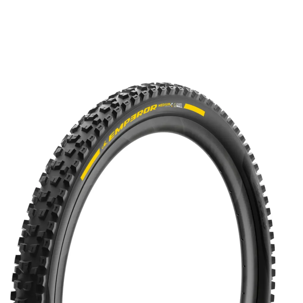 Un primer plano de una cubierta negra para bicicleta de montaña con la inscripción «EMPEROR», que presenta un dibujo profundo de la banda de rodadura y el logotipo amarillo en el flanco, lo que recuerda al diseño robusto de los neumáticos Pirelli Scorpion para MTB, ideales para afrontar senderos con pendientes pronunciadas.