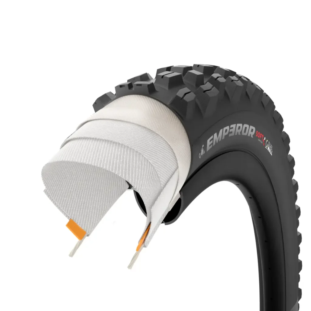 Sección transversal de una cubierta negra para bicicleta de montaña con la inscripción «EMPEROR», en la que se aprecian las capas de su estructura interna y el dibujo de la banda de rodadura, inspirada en neumáticos de MTB de alta gama, como los de la serie Scorpion de Pirelli.