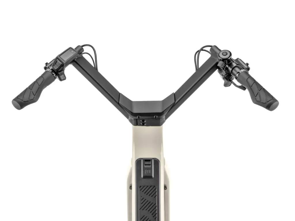 Vista superior del manillar de una bicicleta eléctrica «Moustache Lundi 27», con pantalla digital y mandos en los puños, montado en un cuadro de color beige: ideal para moverse por la ciudad con estilo y comodidad.