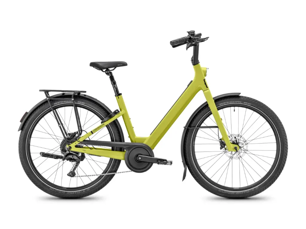 Se muestra de perfil, sobre un fondo blanco, una bicicleta eléctrica Moustache Lundi 27 de cuadro abierto de color amarillo, con neumáticos negros, guardabarros y un portaequipajes trasero: perfecta para moverse por la ciudad con estilo y comodidad.