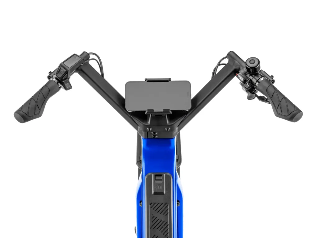 Vista aérea del manillar de una bicicleta eléctrica «Moustache Lundi 27», que cuenta con una pantalla digital, un smartphone acoplado y botones de control en cada puño, con el característico cuadro azul visible en la parte inferior: perfecta para moverse por la ciudad con estilo.