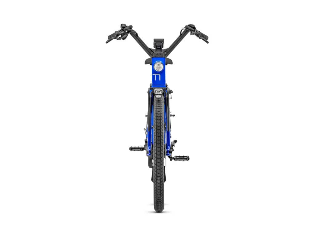 Vista frontal de la bicicleta eléctrica Moustache Lundi 27 azul, con manillar ancho, neumáticos de banda de rodadura gruesa y faro delantero incorporado, sobre un fondo blanco liso: perfecta para recorrer la ciudad con estilo.