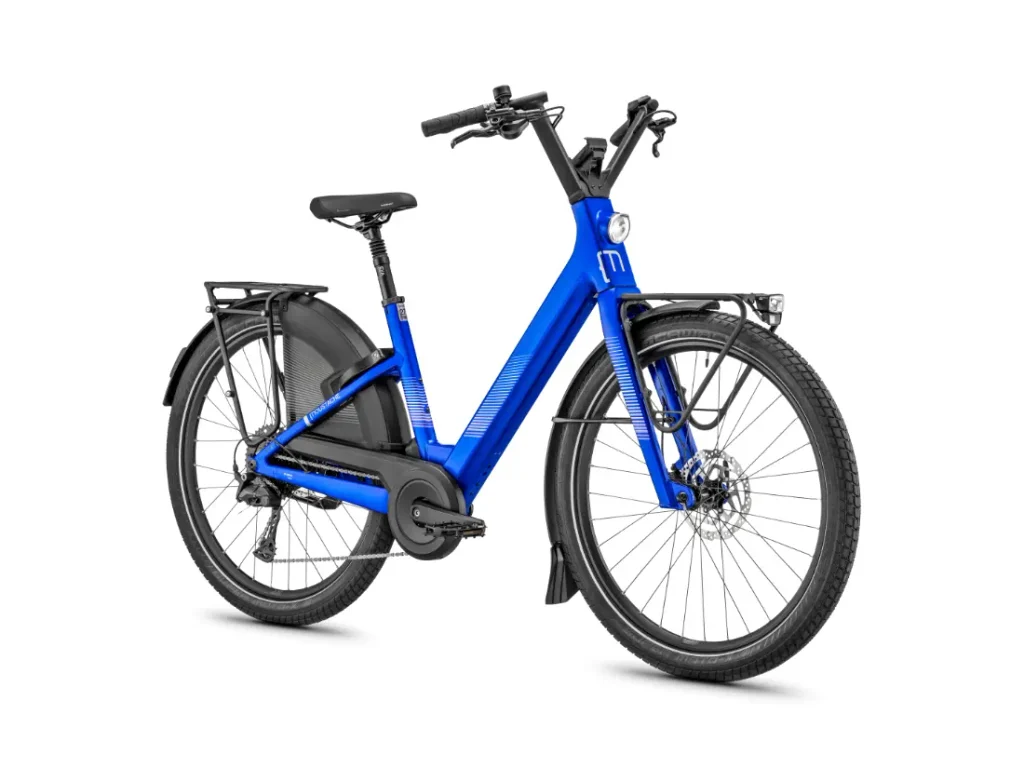 Bicicleta eléctrica «Blue Moustache Lundi 27» con portaequipajes delantero y trasero, guardabarros, horquilla de suspensión delantera, faro delantero y manillar recto —ideal para los desplazamientos urbanos— representada sobre un fondo blanco.