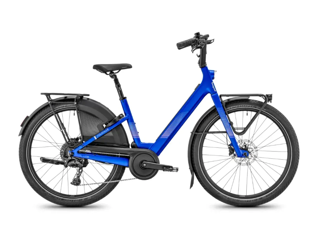 Bicicleta eléctrica «Blue Moustache Lundi 27», con cuadro de acceso fácil, portaequipajes delantero y trasero, guardabarros y frenos de disco —perfecta para los desplazamientos urbanos—, vista de perfil sobre un fondo blanco.