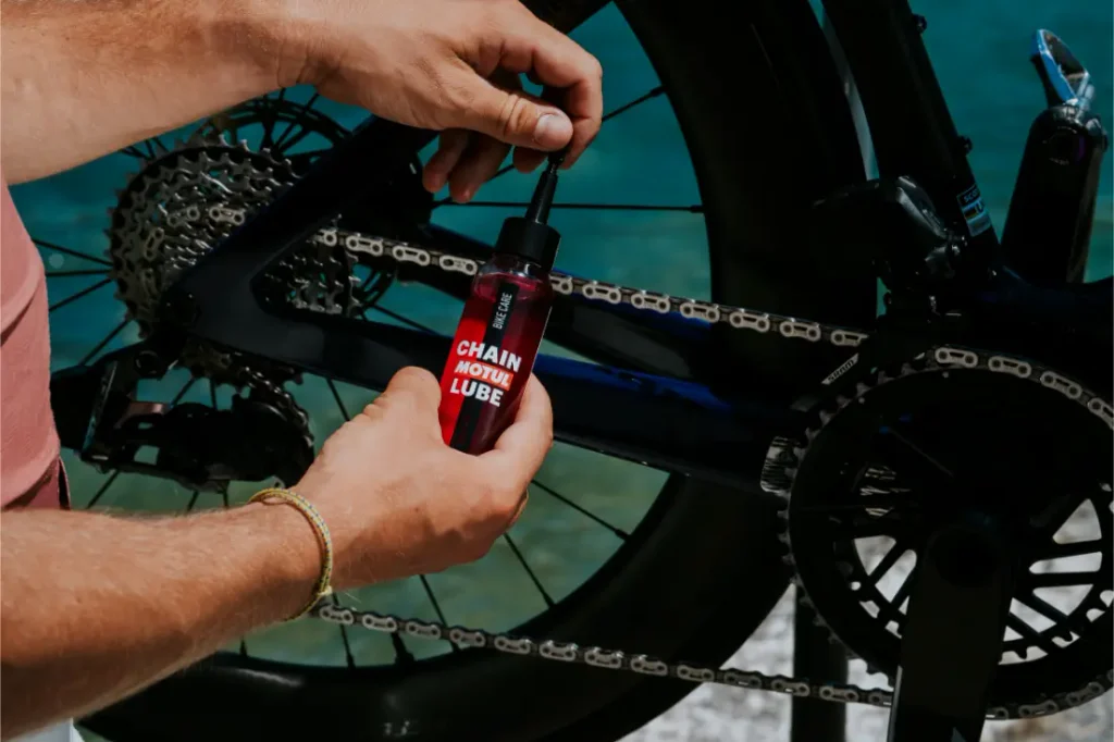 Una persona aplica lubricante para cadenas a la cadena de una bicicleta con un frasco pequeño, centrándose en el mantenimiento del sistema de transmisión de la bicicleta.