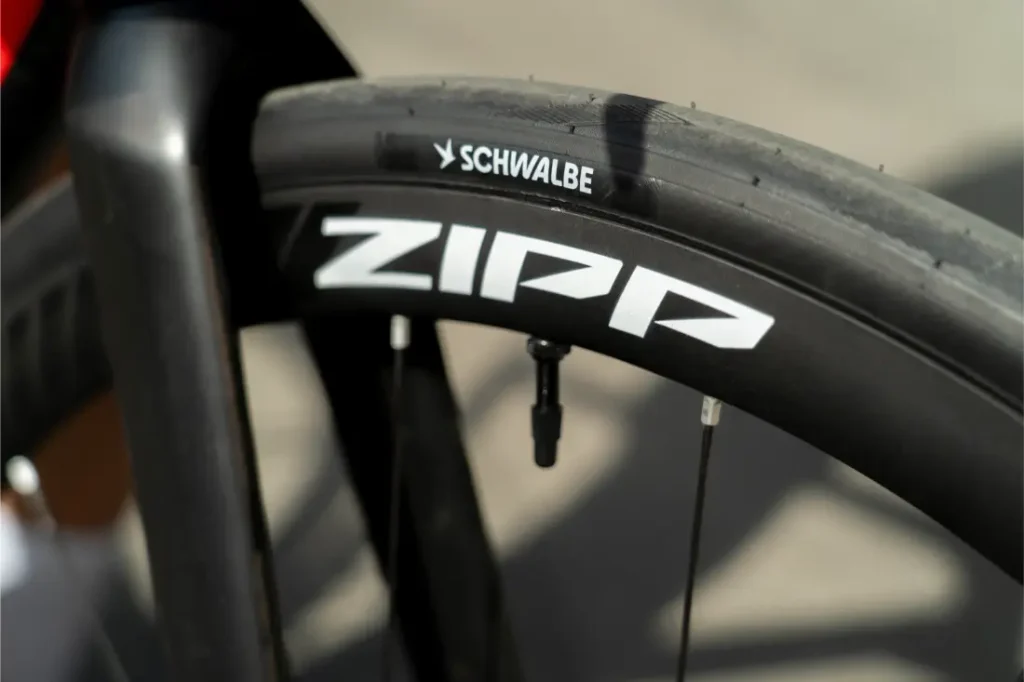 Primer plano de una rueda de bicicleta en el que se aprecia una llanta Zipp y un neumático Schwalbe Pro One Aero, con parte de la horquilla y los radios a la vista.