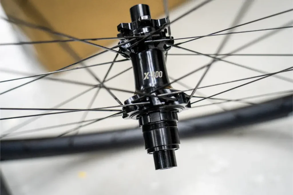 Primer plano de un buje de bicicleta negro con la inscripción «X-300» y radios que se extienden radialmente, montado en una rueda KFX i30 de la reconocida gama Ruedas FSA, sobre un fondo desenfocado, que pone de manifiesto la precisión y el control totales en cada detalle.