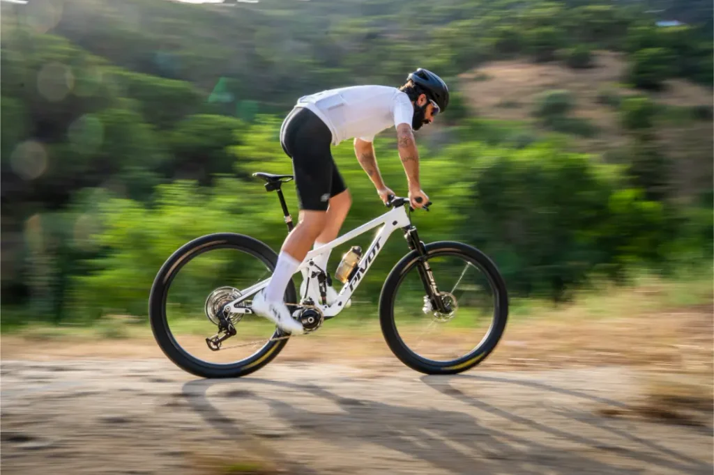 Una persona que lleva casco y equipación de ciclismo recorre a gran velocidad una bicicleta de montaña KFX i30 por un camino de tierra, con árboles verdes al fondo, manteniendo un control total sobre el terreno accidentado gracias a las ruedas FSA de alto rendimiento.
