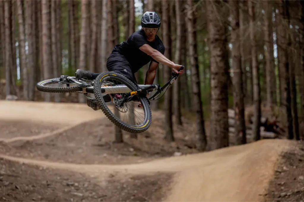 Una persona que lleva casco realiza un salto en una bicicleta de montaña equipada con neumáticos Pirelli Scorpion MTB por un sendero de tierra en un bosque.
