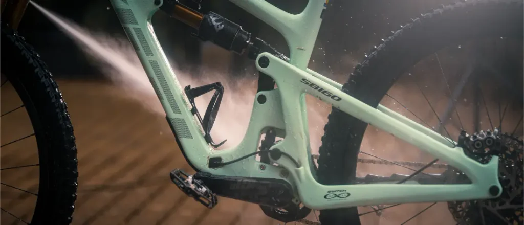 Una bicicleta de montaña de color verde claro a la que le están echando agua con una manguera.