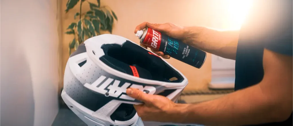 Unas manos rociando limpiador en espuma en el interior de un casco de moto blanco.