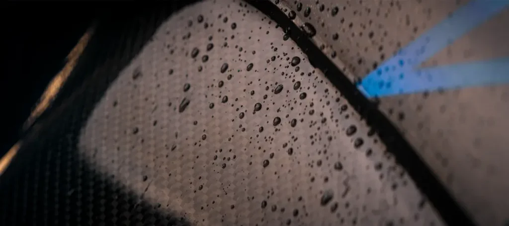 Gotas de lluvia sobre una superficie oscura de fibra de carbono con una línea azul que destaca.
