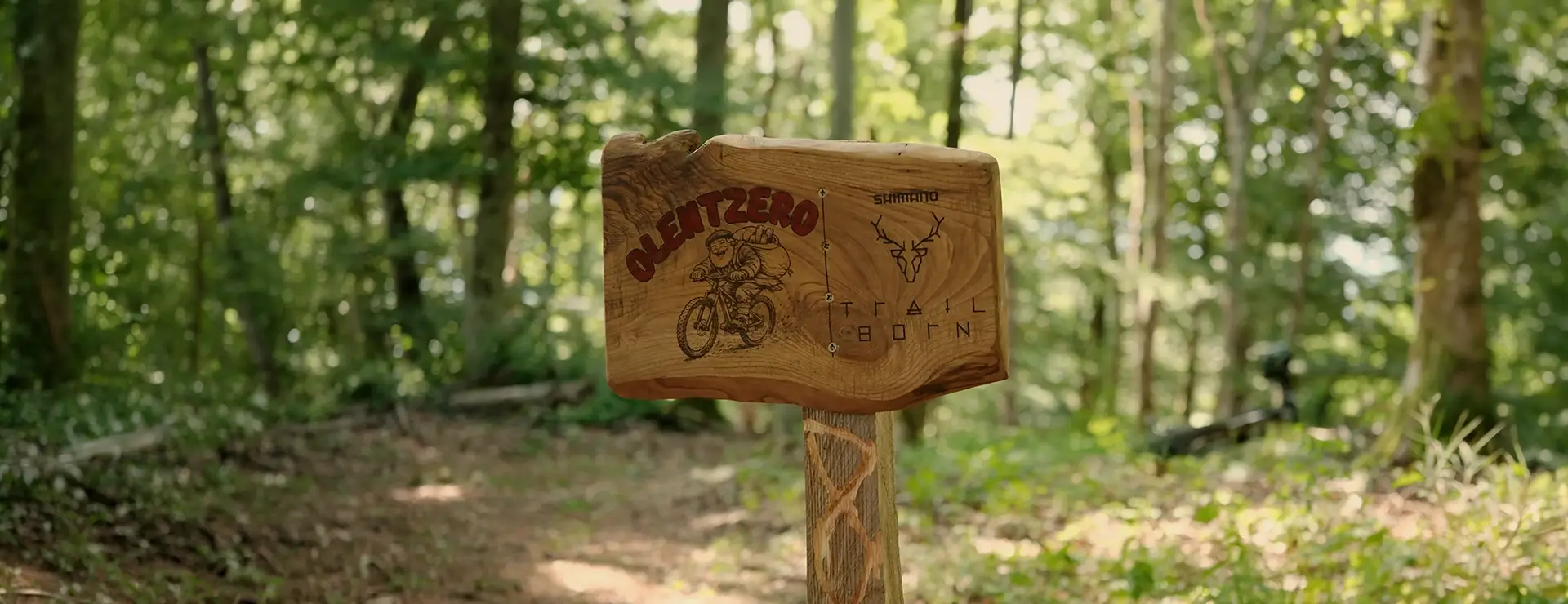 Un cartel de madera situado en la ruta de BTT «Olentzero» de Basaburua en el que se lee «Olentzero» y «Trail Born», junto con la ilustración de una figura montada en una bicicleta de montaña.