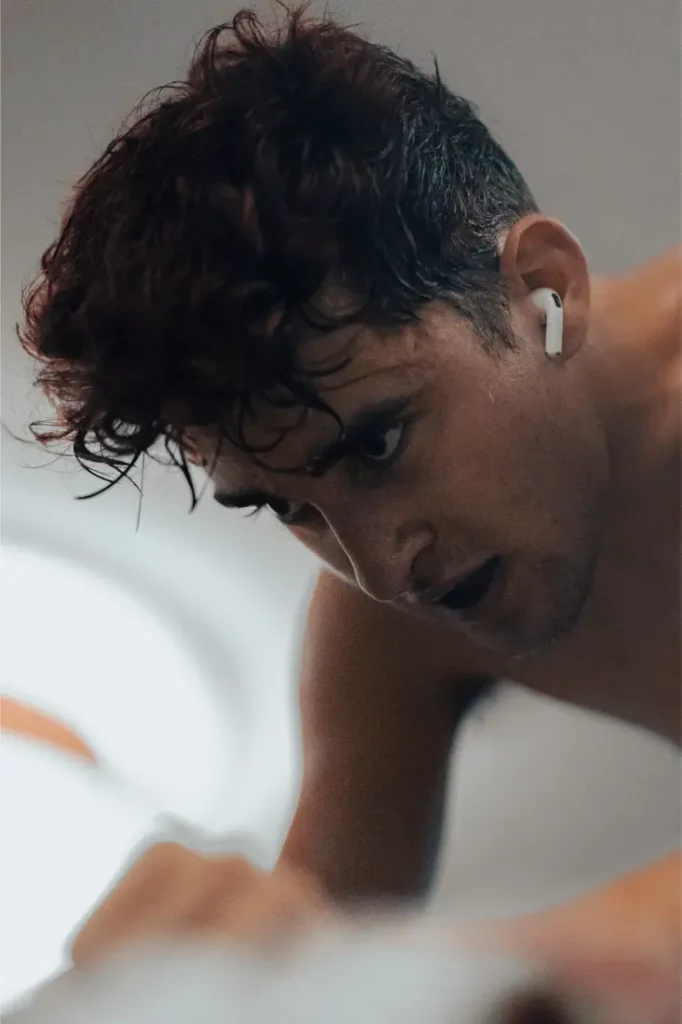Una persona con el pelo húmedo y ondulado y un auricular que mira hacia abajo con la boca abierta, que recuerda al protagonista de *El delfín adolescente*, de Paul Seixas.