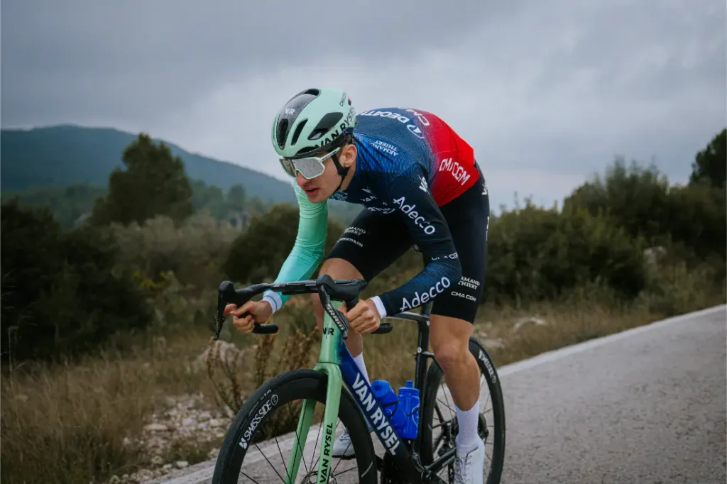 El ciclista profesional Paul Seixas, apodado «el delfín adolescente», pedalea en una bicicleta de carreras de la marca Van Rysel por una carretera asfaltada.