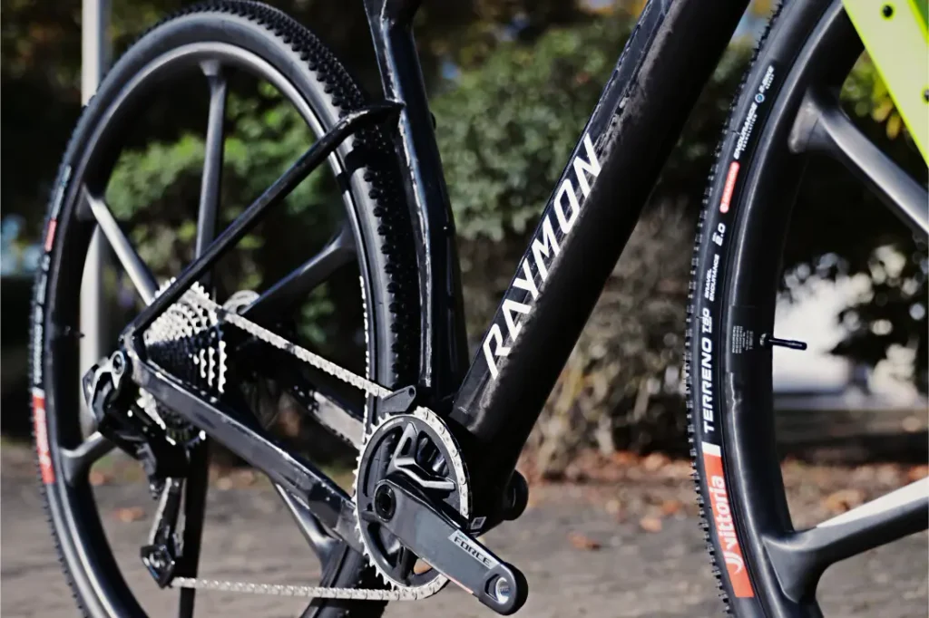 Primer plano de un prototipo de cuadro negro de bicicleta de grava RAYMON con un juego de bielas SRAM Force y neumáticos Vittoria Terreno.
