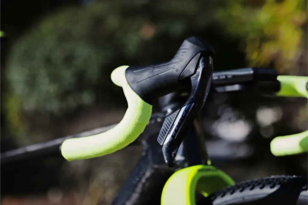 Primer plano de un manillar de bicicleta de grava RAYMON con cinta de color amarillo brillante y una palanca de cambios negra.