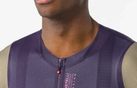 Una persona que lleva un maillot Castelli Corretto LS de manga larga de color morado, con cremallera frontal y mangas grises, fotografiada desde los hombros hacia arriba sobre un fondo liso.