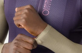 Una persona que lleva un maillot Corretto LS con textura y cremallera se ajusta la manga. El maillot de manga larga es de color morado con la manga en beige y luce el logotipo y el texto de Castelli en el pecho, lo que evoca la comodidad y el diseño aerodinámico de la colección Castelli Transition.