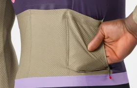 Una persona mete la mano en el bolsillo trasero de un maillot Corretto LS de color beige y morado, mostrando la textura, la elasticidad y el diseño de manga larga del tejido.