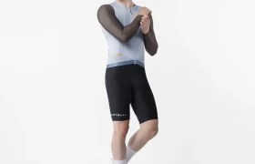 Una persona posa sobre un fondo blanco con un maillot de ciclismo sin mangas, pantalones cortos negros, calcetines blancos y zapatillas de ciclismo, mientras se ajusta el brazo derecho como si se estuviera preparando para ponerse encima el maillot Corretto LS y así ganar en comodidad durante las salidas con manga larga.