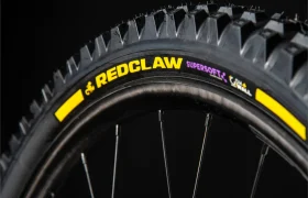 Primer plano de una rueda de bicicleta en el que se aprecia la banda de rodadura y la inscripción «REDCLAW SUPERSOFT» en el flanco negro con detalles en amarillo, sobre un fondo oscuro: ideal para ciclistas que buscan neumáticos de MTB de alto rendimiento inspirados en tecnologías presentes en modelos como el Pirelli Scorpion.