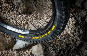 Primer plano de una rueda de bicicleta de montaña con la inscripción «BLACKS KING», con el diseño propio de los neumáticos de MTB de alta gama, apoyada sobre un terreno rocoso y cubierto de grava.