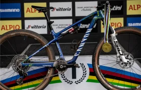 Una bicicleta de montaña Canyon con una medalla de oro colgando del manillar, que recuerda las victorias de Jenny Rissveds, se exhibe frente a un fondo de podio con múltiples logotipos de patrocinadores.