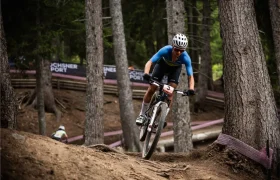 Jenny Rissveds, con casco y equipación azul, monta en bicicleta de montaña por un sendero forestal durante una carrera.