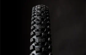 Primer plano de una rueda de bicicleta de montaña negra con relieve, como los neumáticos Pirelli Scorpion MTB, sobre un fondo oscuro y liso.