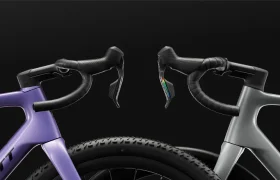Dos manillares de bicicleta de carretera, uno morado y otro gris, aparecen colocados uno al lado del otro sobre un fondo negro, con las ruedas delanteras y las palancas de freno a la vista. Esta composición evoca el espíritu polivalente de la SCOTT Addict Gravel 2027, que ofrece un agarre cómodo para largas rutas por terrenos variados.