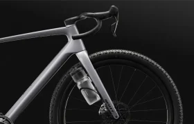 Primer plano de una moderna SCOTT Addict Gravel 2027 de color gris, centrado en la parte delantera, en el que se aprecian el manillar curvo, el bidón y la rueda con textura sobre un fondo negro: una cómoda bicicleta de gravel ideal para cualquier aventura.