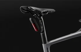 Primer plano del sillín, la tija del sillín y el cuadro de una bicicleta SCOTT Addict Gravel 2027, de colores negro y gris, en la que destaca una luz trasera roja montada debajo del sillín; esta bicicleta es conocida por su diseño polivalente y cómodo, y aparece sobre un fondo oscuro.