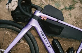 Un primer plano del cuadro morado de la bicicleta SCOTT Addict Gravel 2027 destaca su diseño polivalente, con dos bidones y unas pequeñas flores rosas metidas en la bolsa del tubo superior.