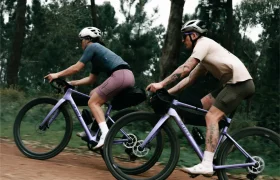 Dos ciclistas, equipados con casco y ropa deportiva, pedalean en unas bicicletas SCOTT Addict Gravel 2027 de color morado por un camino de tierra que atraviesa una zona boscosa, disfrutando de una experiencia ciclista cómoda y versátil.