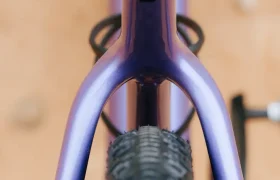 Primer plano desde arriba de un cuadro morado de bicicleta de gravel, con especial atención a la rueda trasera y a los tirantes del sillín, y con un suelo de tierra difuminado al fondo: un aspecto emblemático para una bicicleta polivalente como la SCOTT Addict Gravel 2027.