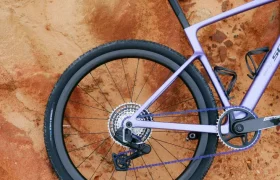 Rueda trasera y sillín de una bicicleta de gravel morada, posiblemente una SCOTT Addict Gravel 2027 polivalente, apoyada sobre un terreno rocoso de color marrón rojizo, vista desde arriba.