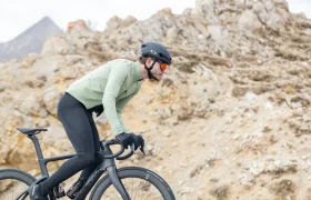 Un ciclista, que lleva casco y gafas de sol, sube en una bicicleta de carretera negra por un sendero rocoso al aire libre.