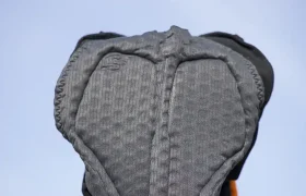 Una mano sostiene un pantalón corto de ciclismo acolchado de color negro contra un cielo azul claro, que recuerda la calidad y la comodidad que se encuentran en la equipación de EQUIPE RS Johdah y chaqueta ASSOS.
