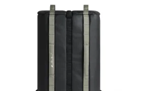 Una mochila rectangular negra con dos correas verdes verticales y tirantes negros, que se muestra en posición vertical sobre un fondo blanco. Diseñada para ciclistas, esta pieza ASSOS x Db es perfecta para tus esenciales del sistema de viaje.