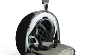 Un casco protector guardado dentro de una funda de transporte ASSOS x Db abierta y con cremallera, con una sección de malla y correas internas visibles, perfecta para los ciclistas que buscan un práctico sistema de viaje.
