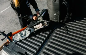 Un ciclista mete un par de zapatos en una bolsa en el maletero de una camioneta, junto con otros enseres y una bicicleta, mostrando el sistema de viaje ASSOS x Db.