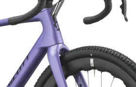 Primer plano de una bicicleta SCOTT Addict Gravel 2027 de color morado en el que se aprecian el manillar curvo, las palancas de freno delanteras y la rueda delantera con banda de rodadura de tacos: características perfectas para una «gravel cómoda» y una bicicleta polivalente.