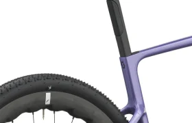 Primer plano de un sillín negro, una tija de sillín y una rueda trasera, en el que se aprecia el cuadro morado de la bicicleta SCOTT Addict Gravel 2027 y la banda de rodadura de los neumáticos con tacos: detalles perfectos para quienes buscan una bicicleta cómoda y polivalente.