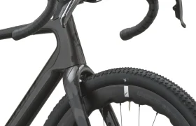 Primer plano de una bicicleta de carretera SCOTT Addict Gravel 2027 negra en el que se aprecian el manillar, las palancas de freno, la rueda delantera y parte del cuadro de carbono, con el dibujo de la banda de rodadura de la rueda visible. Esta bicicleta polivalente combina un diseño elegante con la comodidad para los ciclistas que buscan una bicicleta cómoda en cualquier terreno.