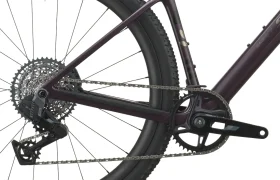 Primer plano de la rueda trasera, la cadena, los cambios y el juego de bielas de una SCOTT Addict Gravel 2027. El cuadro es de color morado oscuro y el neumático lleva la inscripción «Schwalbe G-One R». Esta bicicleta de gravel, polivalente y cómoda, ofrece un equilibrio perfecto entre rendimiento y versatilidad gracias a sus componentes de alta calidad.