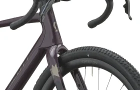 Primer plano de la rueda delantera, la horquilla y el manillar curvo de una bicicleta SCOTT Addict Gravel 2027 de color oscuro, con neumáticos texturizados y la marca «SYNCROS» en la llanta, lo que pone de manifiesto su diseño cómodo y versátil.