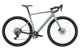 Se muestra de perfil, sobre un fondo blanco, una bicicleta de gravel SCOTT Addict Gravel 2027 de color verde mate, con manillar curvo, sillín negro y neumáticos grandes y con tacos, lo que resalta su diseño polivalente.