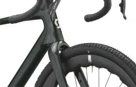 Primer plano de la rueda delantera, la horquilla y el manillar curvo de una cómoda bicicleta gravel, con cinta de manillar negra. La rueda presenta una banda de rodadura con tacos, y el cuadro lleva el logotipo «SCOTT Addict Gravel 2027».