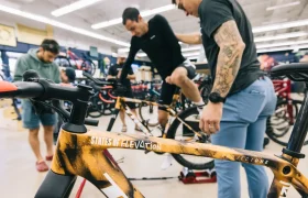 Un hombre monta en una bicicleta en el interior mientras otros dos observan y ayudan; se ven varias bicicletas en el fondo de la tienda States of Elevation - Kilian Jornet.